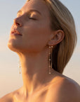 Profile view of a blond woman outdoors with her eyes closed, wearing long gold diamond station threader earrings.