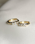 Two small gold huggie hoop earrings, each with three clear round stones, on a white satin-like fabric.