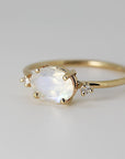 A gold ring with an oval moonstone and two small diamonds on each side, set against a plain white background.