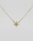 A gold chain necklace with a small, flat, eight-point star pendant, encrusted with tiny clear stones, against a plain white background.