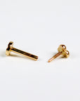 Disassembled gold flat back labret stud showing the threaded post and trinity ball top separated on a white surface.