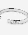 A polished silver-colored metal open cuff bracelet displayed alone on a plain white background with engraved rune symbols near one end.