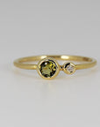Front view of the yellow gold dual birthstone ring showcasing the large round green tourmaline next to the smaller round diamond in bezel settings.