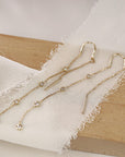 Two long gold diamond threader earrings laid across a piece of white frayed fabric and a wooden block.