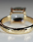 The back of the gold ring resting on a white surface, displaying the hammered texture of the band with the main stone blurred in the background.