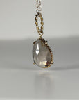 Side angle view of a pear-shaped faceted smokey quartz gemstone in a twisted gold setting suspended on a chain.