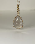 Front view of a faceted pear-shaped smokey quartz gemstone set in twisted gold against a plain surface.