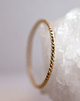 A side view of a thin gold twisted ring standing upright against a textured white quartz crystal background.
