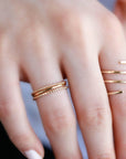 A hand showing three stacked gold rings on one finger and a spiral wrap ring on an adjacent finger.