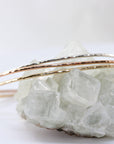 Three thin hammered metal cuff bracelets in silver, rose gold, and yellow gold rest on a rough crystal cluster.