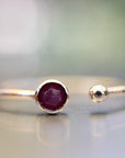 Low-angle shot of the gold ring on a reflective surface, highlighting the hexagonal rose-cut ruby and spherical ball terminal.