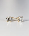 Two round brilliant-cut diamond stud earrings in yellow gold settings displayed on a light surface.