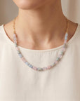 A person wearing a gemstone tube necklace with a gold chain portion against a white top.
