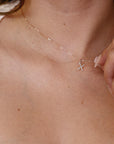 A person wearing a delicate gold chain necklace with a diamond-paved letter X pendant.