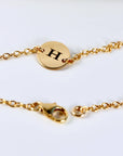 A gold chain bracelet with a lobster clasp and a circular disk engraved with the letter H.