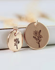 Two rose gold disc pendants of different sizes with engraved flower designs, displayed in front of a white surface.