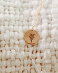 A gold chain necklace with a round engraved flower disc pendant lying on a white textured blanket.