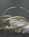 A large stack of thin yellow gold cuff bracelets is displayed over a white crystal cluster against a dark background.