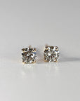Close-up of two sparkling salt and pepper diamond stud earrings in gold prongs against a plain white background.