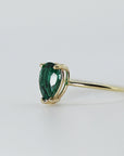 Side-angle view of a gold ring featuring a pear-shaped green stone secured by prongs on a plain gold band.