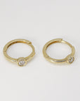 Two small gold hoop earrings with solitaire bezel-set diamonds viewed at a slight angle on a light background.