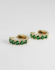 Front view of two gold hoop earrings set with round green gems, resting on a white surface.