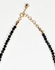 A close-up view of the gold-colored clasp and heart-shaped extender links on a black beaded necklace.