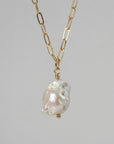 Close-up of a necklace featuring a chunky gold link chain and a single irregular white baroque pearl pendant.