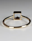 Rear view of a gold ring resting on a white surface with the open back of the square stone setting visible.
