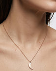 A portrait focusing on the neck and collarbone area of a model wearing a gold crescent moon necklace.