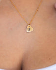 Close-up of a gold heart necklace resting on a person wearing a white top.