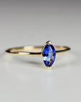 A gold ring with a marquise-cut blue sapphire captured in a slight angle view against a neutral white background.