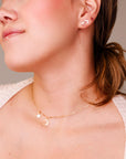 A woman wearing a gold star stud, a crescent moon stud, and a matching charm necklace.