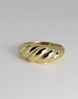 A gold croissant-style ring isolated on a light gray surface.