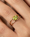 The gold double-band peridot ring is worn on a finger against a neutral fabric background.