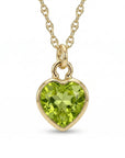 A gold necklace features a faceted heart-shaped light green gemstone pendant centered against a white surface.