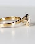 Profile view of a gold bezel-set cushion cut ring resting on a light surface, showing the gallery and band.