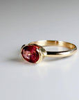 An angled view of the gold ring showcasing the faceted pink tourmaline stone secured horizontally in a bezel setting.