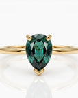 Front view of a gold ring featuring a prong-set pear-cut dark green gemstone on a white surface.