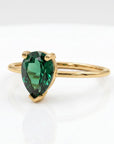 Angled side view of the gold ring with a pear-shaped green gemstone resting on a white background.