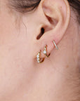 Close-up of a curated ear stack featuring three gold hoop earrings and a delicate pavé helix ring.