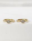 Two gold hoop earrings with bezel-set diamonds displayed upright on a white platform.