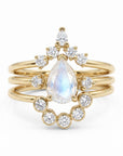 A stack of three gold rings featuring a pear-shaped moonstone center stone and multiple small round diamonds.