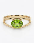 A gold double-band ring featuring a prong-set oval green peridot stone, shown centered on a white background.