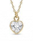 Close up of a gold necklace featuring a faceted heart-shaped clear gemstone pendant hanging from a delicate chain.