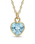A gold chain necklace holds a faceted heart-shaped light blue gemstone pendant against a white background.