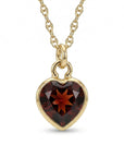 A gold chain necklace holds a faceted heart-shaped dark red gemstone pendant.