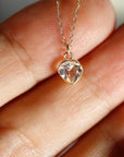 Macro shot of a tiny gold chain and a faceted heart-shaped clear gemstone charm held in a hand.
