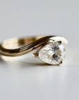 A studio shot of the gold pear-shaped solitaire ring angled on a light gray surface.