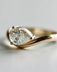 A detailed product shot of the gold pear moissanite ring on a plain surface.